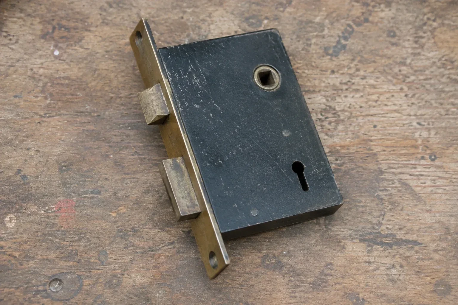 Closed mortise lock case with spindle opening, keyhole, latch and deadbolt on a wooden workbench. — Vintage Mortise Lock Service, Hamilton